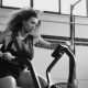 Young woman doing air bike workout in gym, 58x58, Vinilo Adhesivo, Sin Laminado (3 años garantía en exterior/interior), Original, Blanco y negro